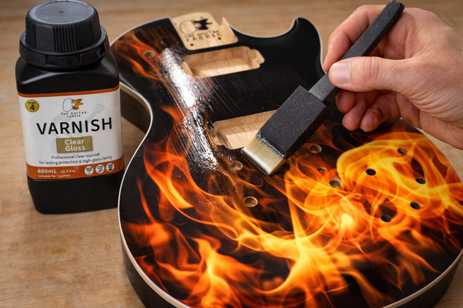 Hand applying water-based clear varnish over a flame vinyl guitar wrap, with The Guitar Fabrik Clear Gloss varnish bottle next to the guitar body.