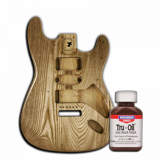 Tru Oil 90mL guitar finish bottle displayed next to unfinished wooden guitar body showing wood grain detail